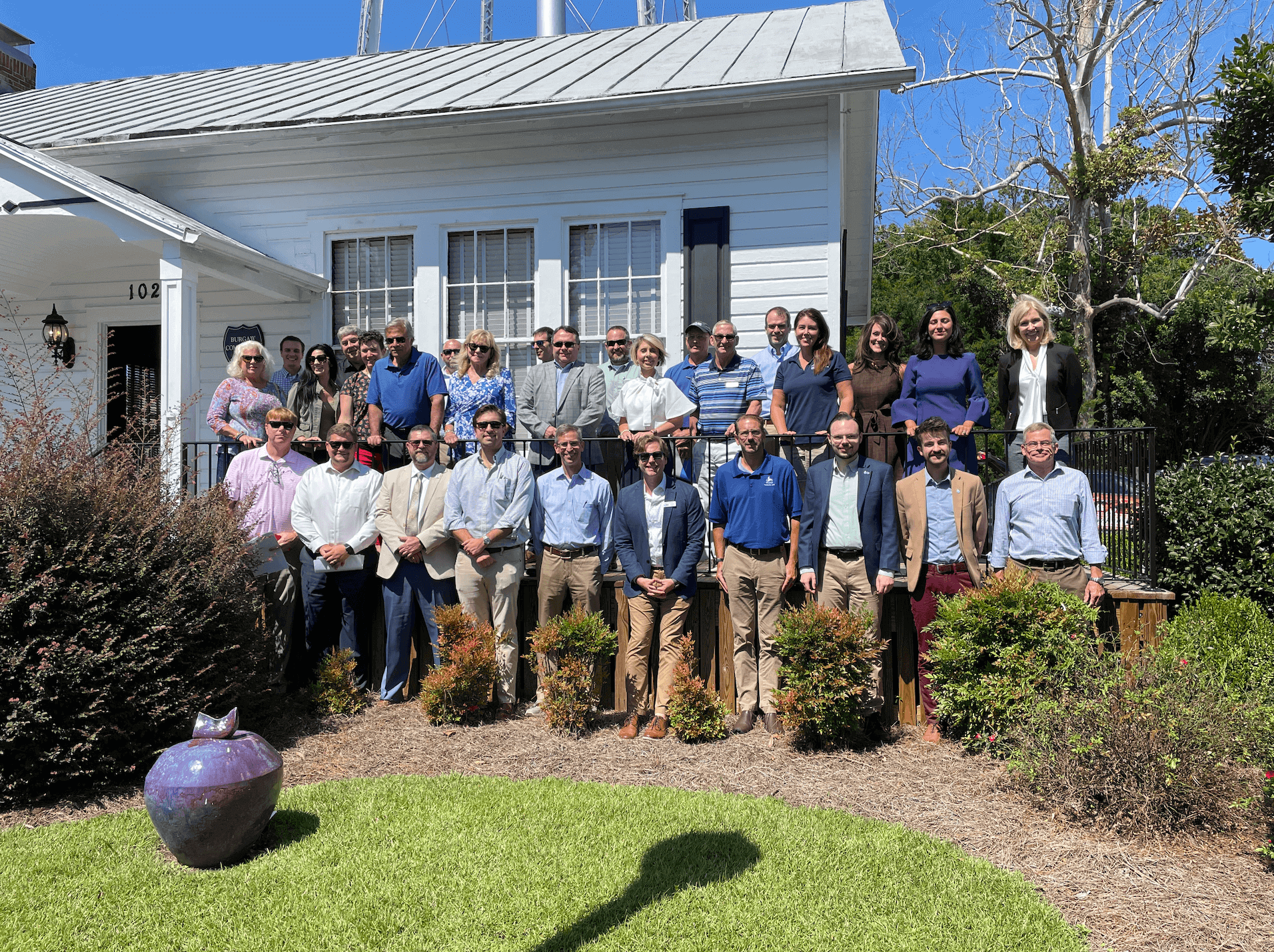 group poses for photo on deck of a white house.