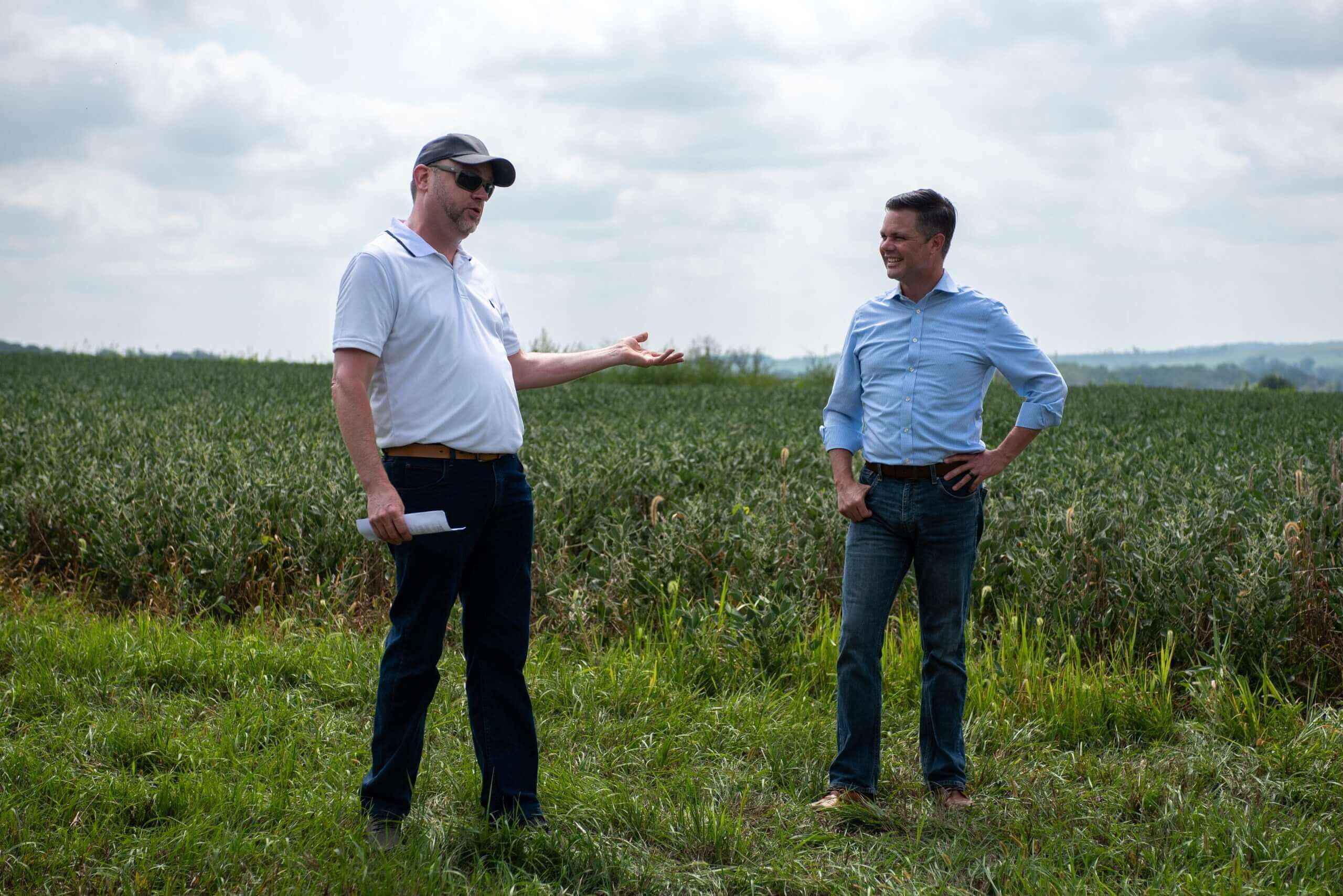 two men talking in front of cropland
